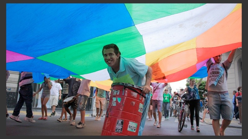 Un joven con su tambor parece disfrutar debajo de una gran bandera multicolor.