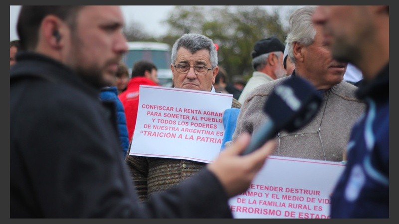 Un hombre muestra un cartel mientras el periodista Pedro Levy hace una entrevista a un productor.