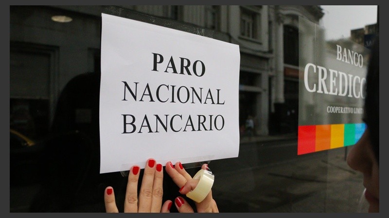 Una empleada pega un cartel en un entidad bancaria. (Alan Monzón/Rosario3.com)