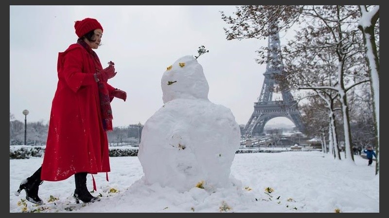 Una mujer arma un muñeco de nieve frente a la torre Eiffel.