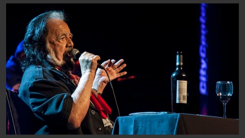 Guaraní canto parado y sentado en una mesa con un buen vino.