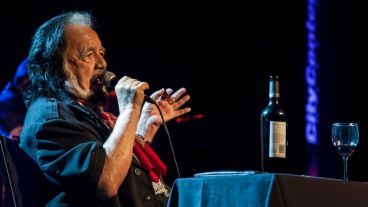 Guaraní canto parado y sentado en una mesa con un buen vino.