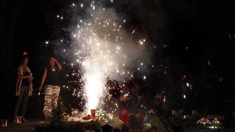 Una familia enciende velas y fuegos artificiales junto a una tumba durante la 