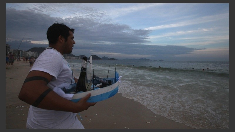 Un joven lleva al mar un barco pequeño con ofrendas de sus fieles.