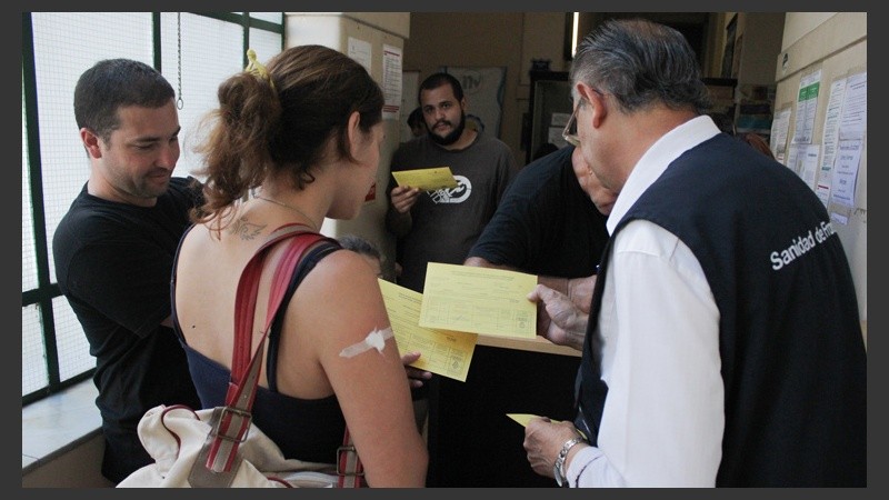 Un hombre le entrega el certificado internacional de vacunación a una joven a punto de viajar a Brasil.
