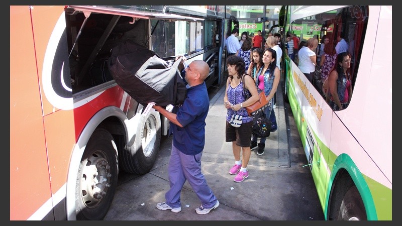 Un maletero sube un bolso mientras los pasajeros esperan detrás.