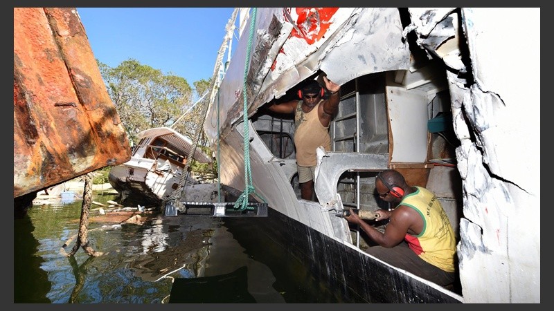 Dos hombres realiza reparaciones en un bote golpeado por otra embarcación durante el paso del ciclón Pam.