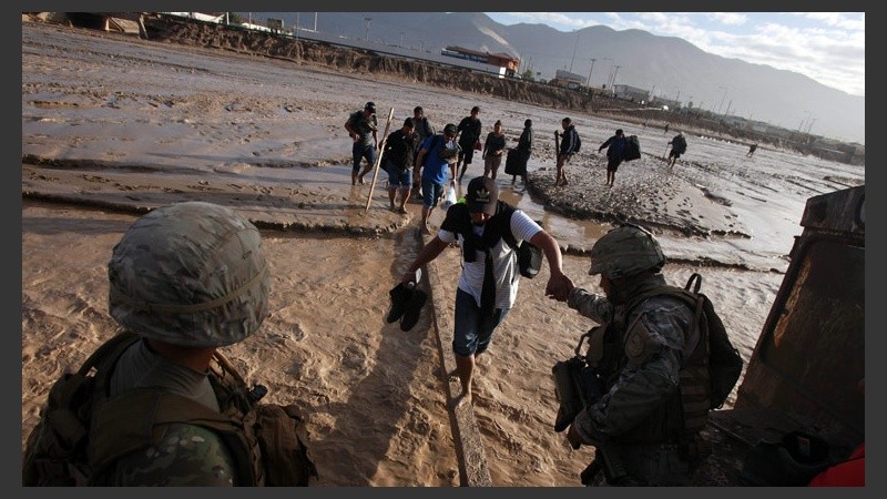 Soldados chilenos ayudan a cruzar el caudal del río a varias personas.