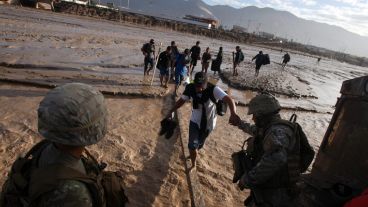 Soldados chilenos ayudan a cruzar el caudal del río a varias personas.