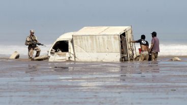 Dos hombres descargan mercancía de un vehículo varado en la playa de Charañal.