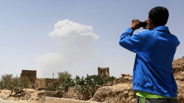 Un hombre fotografía la columna de humo que se alza tras un bombardeo de la coalición árabe.