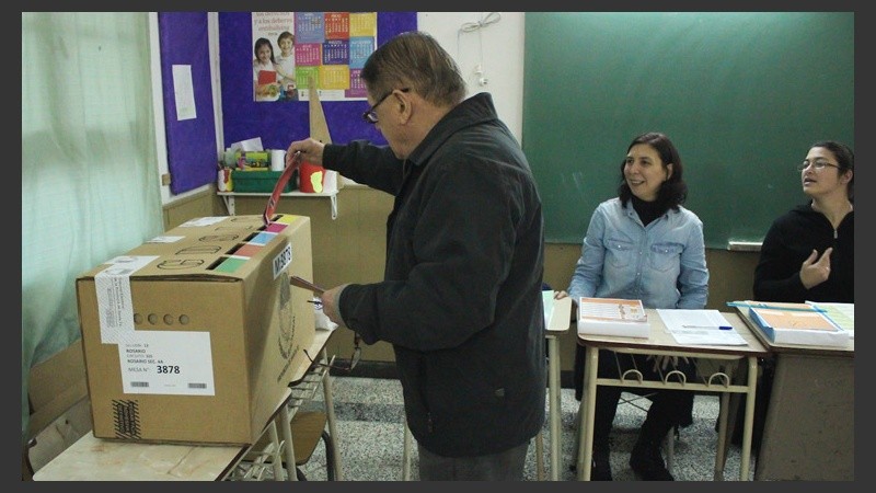 Un hombre deposita su voto ante la mirada atenta de los fiscales.