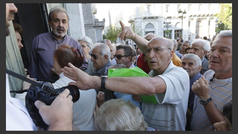 Un jubilado rechaza las fotografías de un fotógrafo mientras espera su turno para recibir su pensión en una sucursal de un banco griego. (EFE)