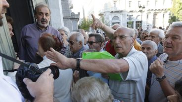 Un jubilado rechaza las fotografías de un fotógrafo mientras espera su turno para recibir su pensión en una sucursal de un banco griego. (EFE)