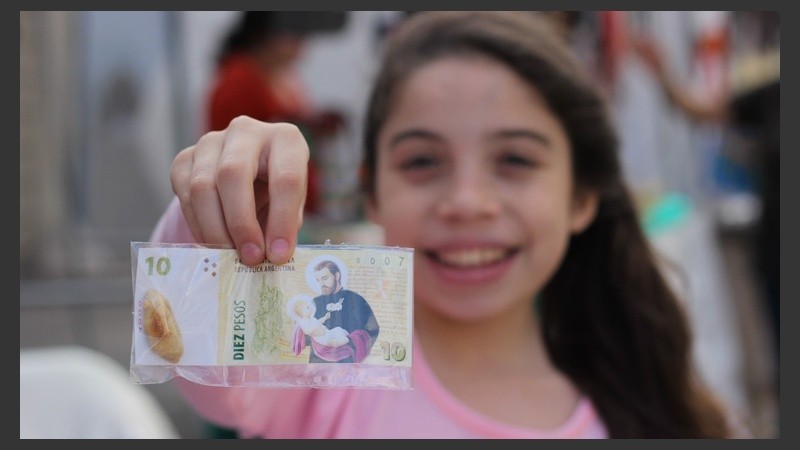 Una joven muestra a cámara un billete con la cara de San Cayetano. (Alan Monzón/Rosario3.com)