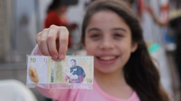 Una joven muestra a cámara un billete con la cara de San Cayetano. (Alan Monzón/Rosario3.com)