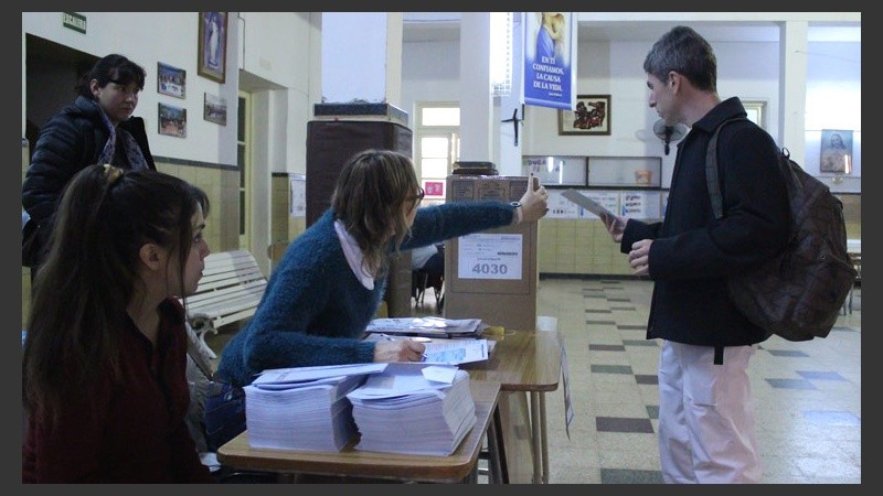 Una autoridad de mesa indica dónde poner el sobre a un elector. (Rosario3.com)