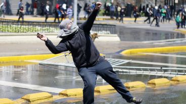 Uno de los jóvenes arroja una piedra a los policías durante los enfrentamientos. (EFE)