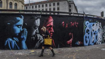 Una mujer camina junto a un grafiti que conmemora a las víctimas realizado por el artista kazajo "ChemiS" en Praga. (EFE)