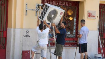 Dos jóvenes instalan un aire acondicionado en un local del centro.