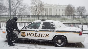 Un policía limpia su auto. Detrás, la Casa Blanca. (EFE)