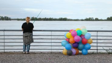 Una mujer pescando junto a unos globos de colores atados a la baranda. (Alan Monzón/Rosario3.com)