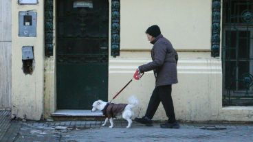 Una señora pasea con su perro abrigado. El frío se siente con fuerza y aún no llegó el invierno. (Rosario3.com)