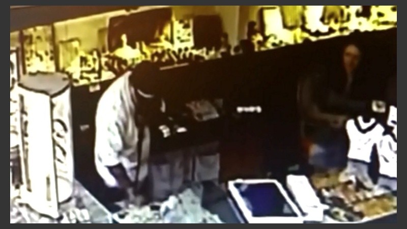 Un asaltante revisa un mostrador. A su derecha, la encargada del local.
