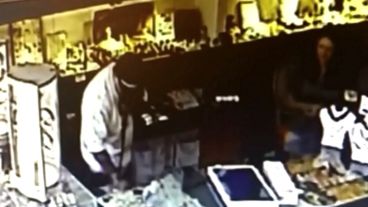 Un asaltante revisa un mostrador. A su derecha, la encargada del local.