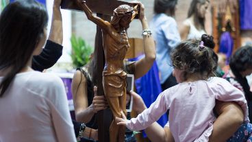 Una madre junto a su pequeña hija tocan la imagen del cristo crucificado