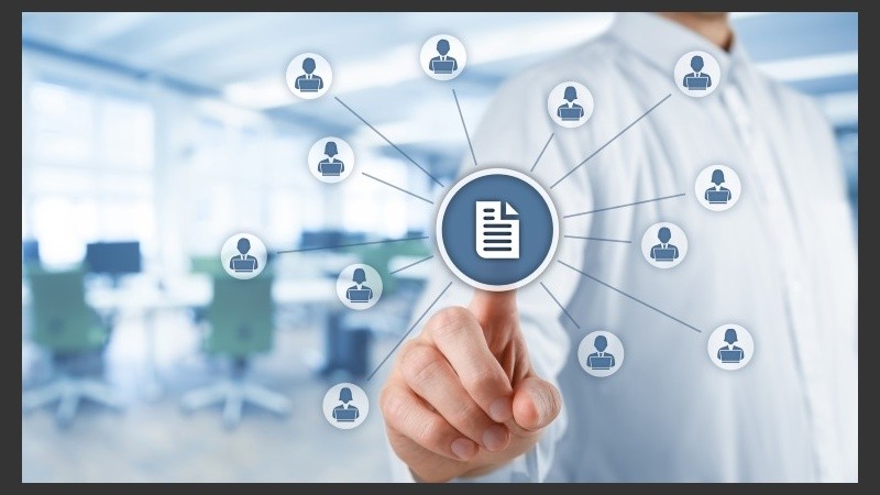 Corporate data management system (DMS) and document management system concept. Businessman click (or publish) on document connected with corporate users working on notebooks with access rights. Wide banner composition with office in background.