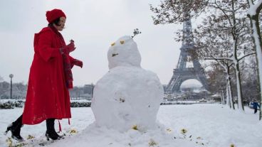 Una mujer arma un muñeco de nieve frente a la torre Eiffel.