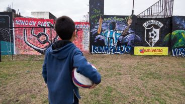 Un niño mira una pintura en el campito donde Messi jugó desde chiquito en la esquina de su casa.