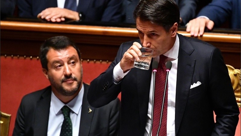 Conte presenta la renuncia y toma agua; Salvini a su lado, observa.
