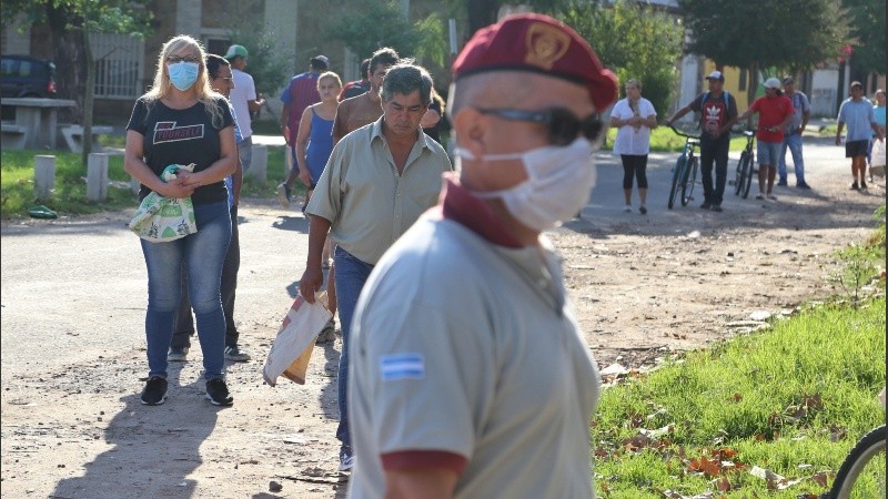 La larga fila de vecinos y vecinas frente a la panadería y la autoridad que intentaba ordenar la cola. 