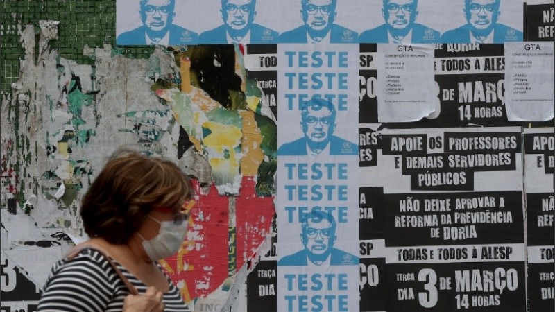 Una mujer con barbijo camina frente a una imagen del líder de la OMS.