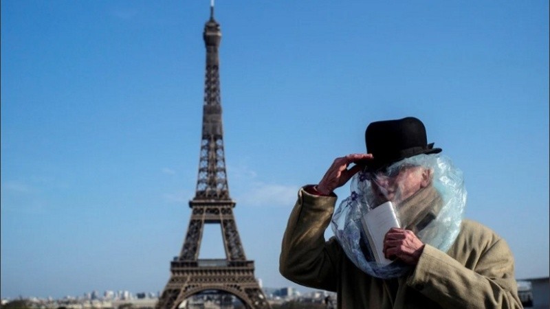Un hombre cubierto con una bolsa de plástico lee un libro frente a la Torre Eiffel en París (Francia), este domingo. 