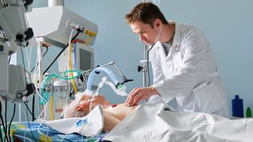 Intensive care caucasian doctor examines intubated critical stance patient writing notes to case report in intensive care department