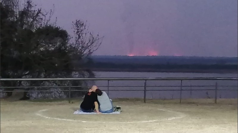Una pareja contempla el atardecer con las llamas de fondo.