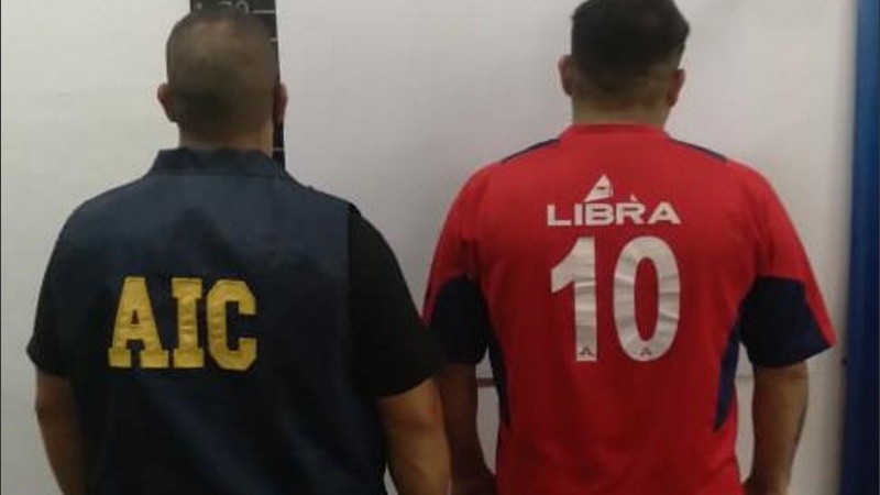 El detenido de espaldas junto a un agente policial. 