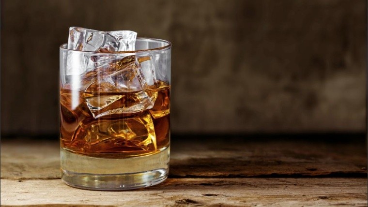 glass of scotch whiskey with ice cubes on a rustic wooden table, copy space in the brown background-Not Released (NR)