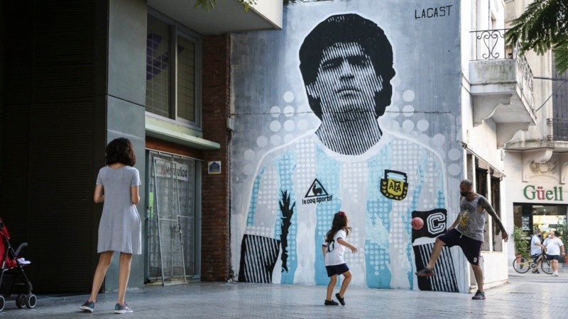Padre e hija juegan a la pelota frente al mural recién terminado de Maradona. 