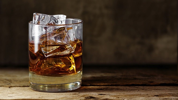 glass of scotch whiskey with ice cubes on a rustic wooden table, copy space in the brown background-Not Released (NR)