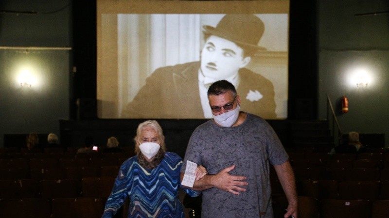 Una mujer mayor sale de vacunarse del brazo de un familiar, con Chaplin de fondo en la pantalla. 