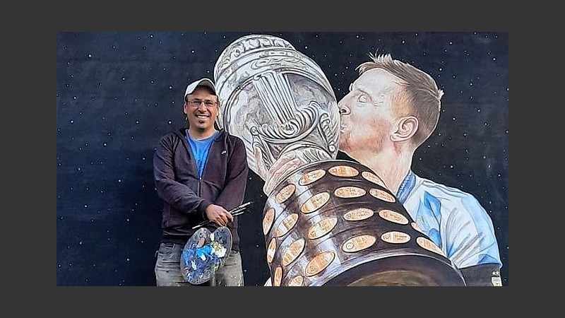 Leo y su anhelado trofeo con la celeste y blanca, en una pared de barrio Alvear.