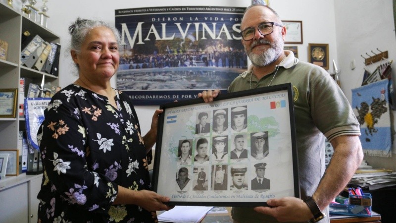 Norma y Fernando sostienen las fotos de los 13 héroes rosarinos de Malvinas, entre ellos Gallo.