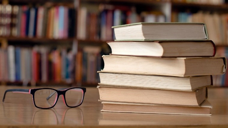 Books and eyeglasses on wooden desk in library.