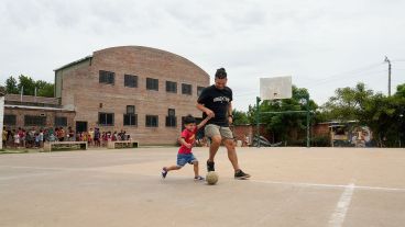 Ezequiel Núñez juega con su hijo de 3 años en el playón frente a la escuela: atrás la cola para el comedor.