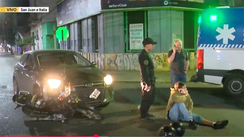 El joven en el piso, al lado los cascos. Y su acompañante arriba de la ambulancia.