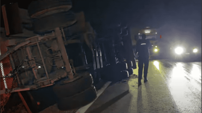 El camionero junto al acoplado de su camión, visiblemente volcado hacia la banquina, mientras pasaban otros vehículos a su lado.